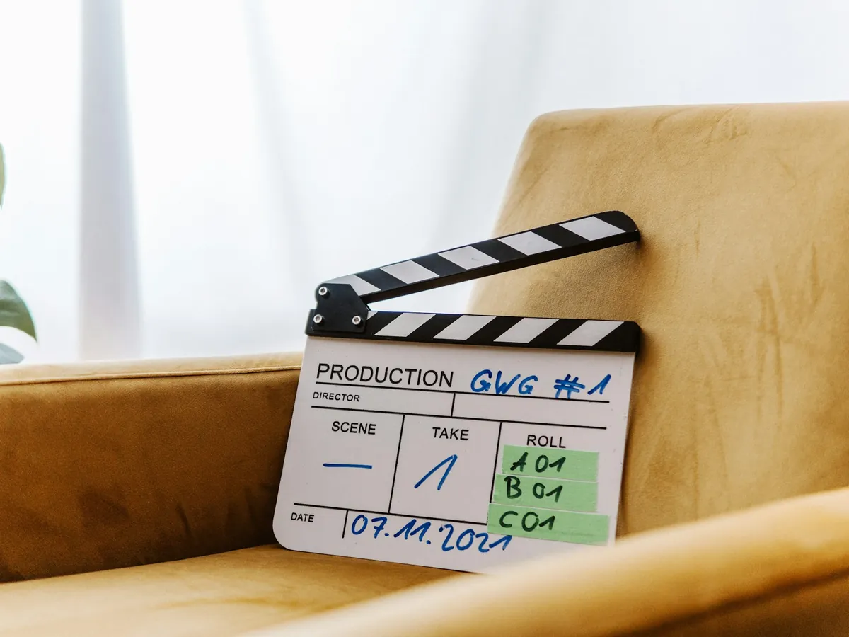 Klaps filmowy oparty o żółty welurowy fotel przy jasnym oknie